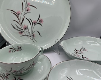 May include: A set of vintage china dinnerware with a delicate floral pattern in shades of pink and brown on a light green background. The set includes a large dinner plate, a smaller plate, a soup bowl, and a teacup and saucer.