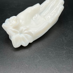 Puede incluir: Una mano de vidrio de leche blanco con una rosa esculpida en la muñeca. La mano está ahuecada, como para sostener algo.