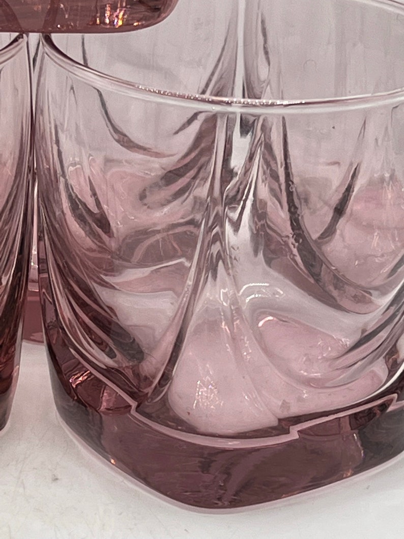 May include: Set of four clear glass tumblers with a swirling, textured design. The glasses have a light pink hue and a square base.