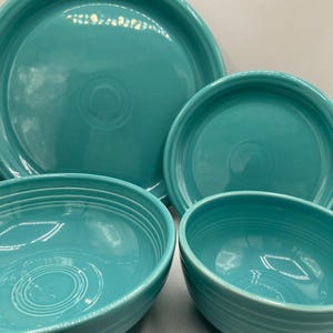 May include: A collection of turquoise ceramic tableware, including a large dinner plate, a smaller plate, and two bowls. The plates and bowls have a glossy finish and concentric circle detailing.