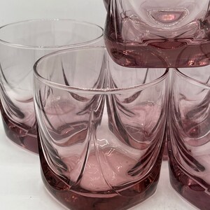 May include: Set of four clear glass tumblers with a pink hue and a unique, wavy design. The glasses are stacked on top of each other.