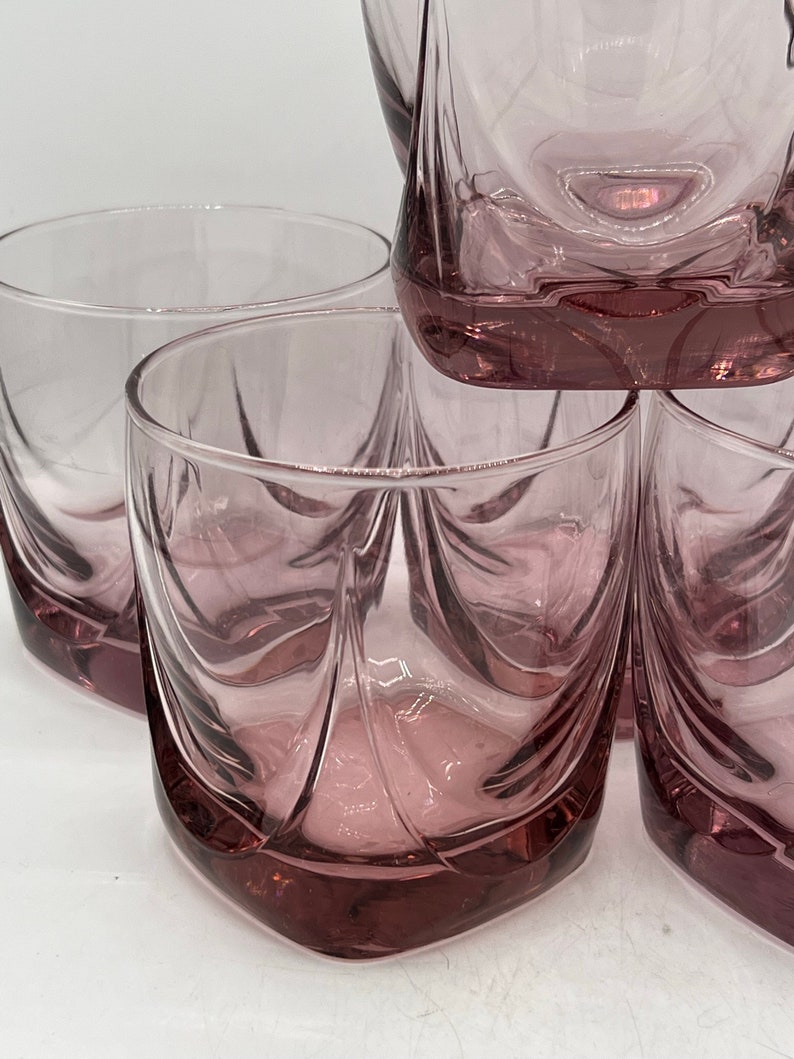 May include: Set of four clear glass tumblers with a pink hue and a unique, wavy design. The glasses are stacked on top of each other.