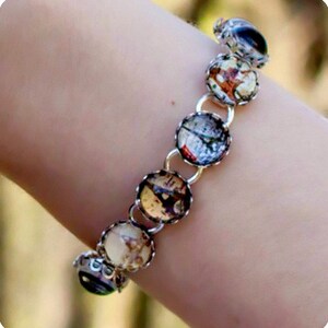 Puede incluir: Un brazalete de cadena de plata con abalorios redondos de vidrio transparente que presentan imágenes vintage. Los abalorios están unidos a la cadena con anillos de plata.