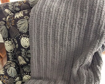 May include: A gray knitted throw blanket with a textured, ribbed pattern is draped over a chair with a floral patterned upholstery.