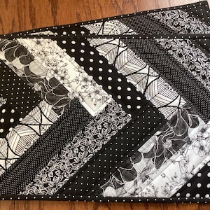 May include: Two black and white quilted placemats with a geometric pattern of black and white floral designs, leaves, and polka dots.