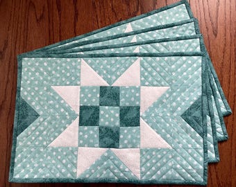 May include: Set of four teal blue quilted placemats with a white star design. The placemats have a white polka dot pattern and a teal blue border.