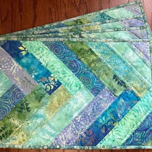 May include: Set of six teal, blue, and green quilted placemats with a diagonal pattern. The placemats have a light green border.