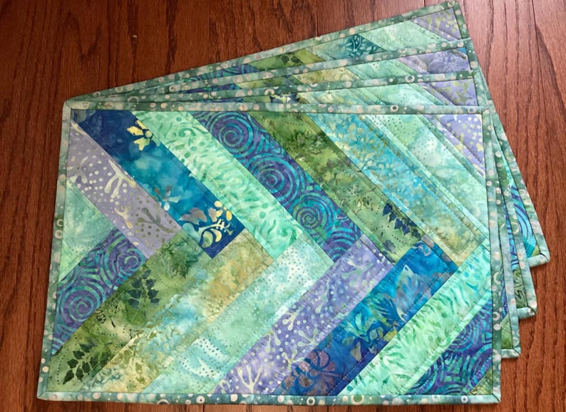 May include: Set of six teal, blue, and green quilted placemats with a diagonal pattern. The placemats have a light green border.