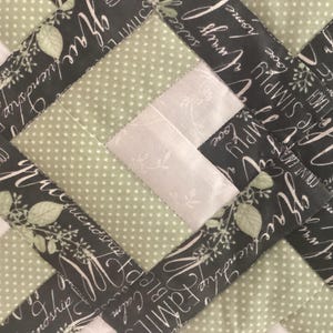 Pode incluir: Uma colcha de retalhos com um padr&atilde;o geom&eacute;trico repetitivo de tecido verde s&aacute;lvia com bolinhas brancas, tecido cinza claro com uma estampa floral branca sutil e tecido cinza escuro com texto branco em cursivo escrito grace, friendship, always.