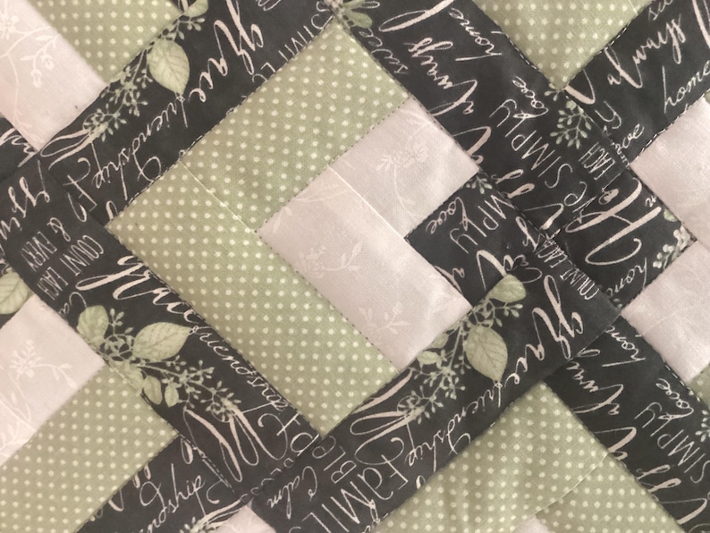 Pode incluir: Uma colcha de retalhos com um padr&atilde;o geom&eacute;trico repetitivo de tecido verde s&aacute;lvia com bolinhas brancas, tecido cinza claro com uma estampa floral branca sutil e tecido cinza escuro com texto branco em cursivo escrito grace, friendship, always.