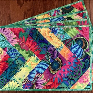 May include: Set of four colorful quilted placemats with a green border. The placemats feature a diagonal pattern of bright floral fabric.