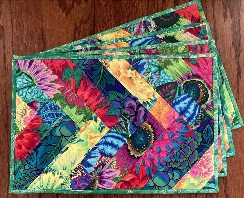 May include: Set of four colorful quilted placemats with a green border. The placemats feature a diagonal pattern of bright floral fabric.