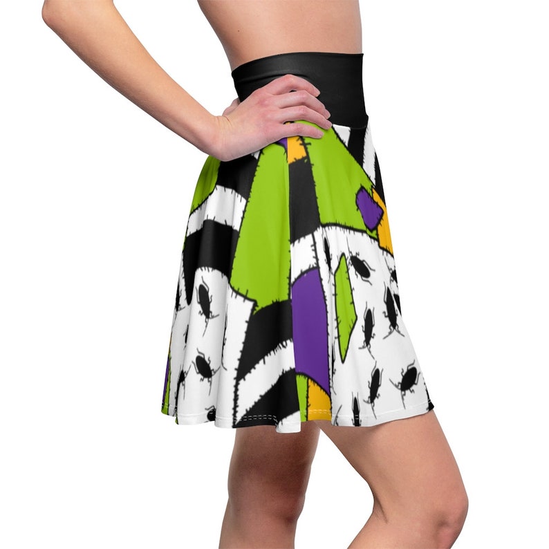 May include: A green, purple, yellow, and black patchwork skirt with a black waistband. The skirt has a white background with black stitching and a pattern of small black bugs.