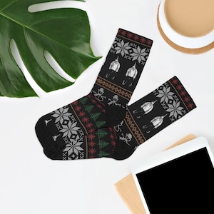 May include: Black socks with a festive pattern featuring snowflakes, snowmen, and Christmas trees. The socks also have a repeating pattern of a person skiing. The socks are a cozy winter accessory.