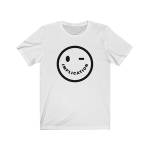 May include: White t-shirt featuring a black smiley face with one eye closed and the word "IMPLICATION" written around it.