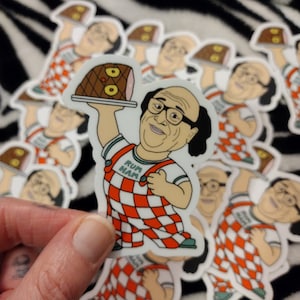 May include: A sticker featuring a cartoon character wearing a red and white checkered jumpsuit and holding a platter with a ham. The character is wearing glasses and has a smile on their face. The text "Rum Ham" is printed on the character's shirt.