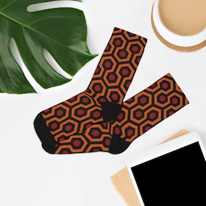 May include: A pair of socks with a repeating geometric pattern in orange, red, and black. The pattern resembles the carpet from the movie "The Shining".