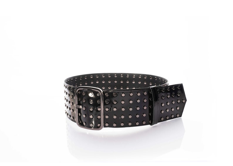 May include: A wide black belt with a glossy finish, featuring multiple rows of small, dark metallic studs across the entire length. The belt includes a large, rectangular, dark metallic buckle and a matching belt loop, creating a uniform look.