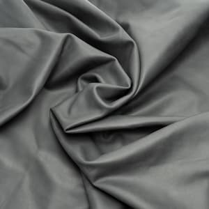 Puede incluir: Una pieza de cuero de color gris oscuro s&oacute;lido con un acabado liso y mate. El material est&aacute; drapeado en pliegues suaves y fluidos, creando sombras y reflejos profundos en la superficie que enfatizan la textura y flexibilidad de la piel.