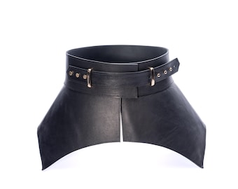 May include: A wide black leather corset belt featuring a structured design with a central vertical split at the bottom. The belt includes a horizontal strap across the midsection secured by a gold-toned metal buckle and multiple adjustment holes.