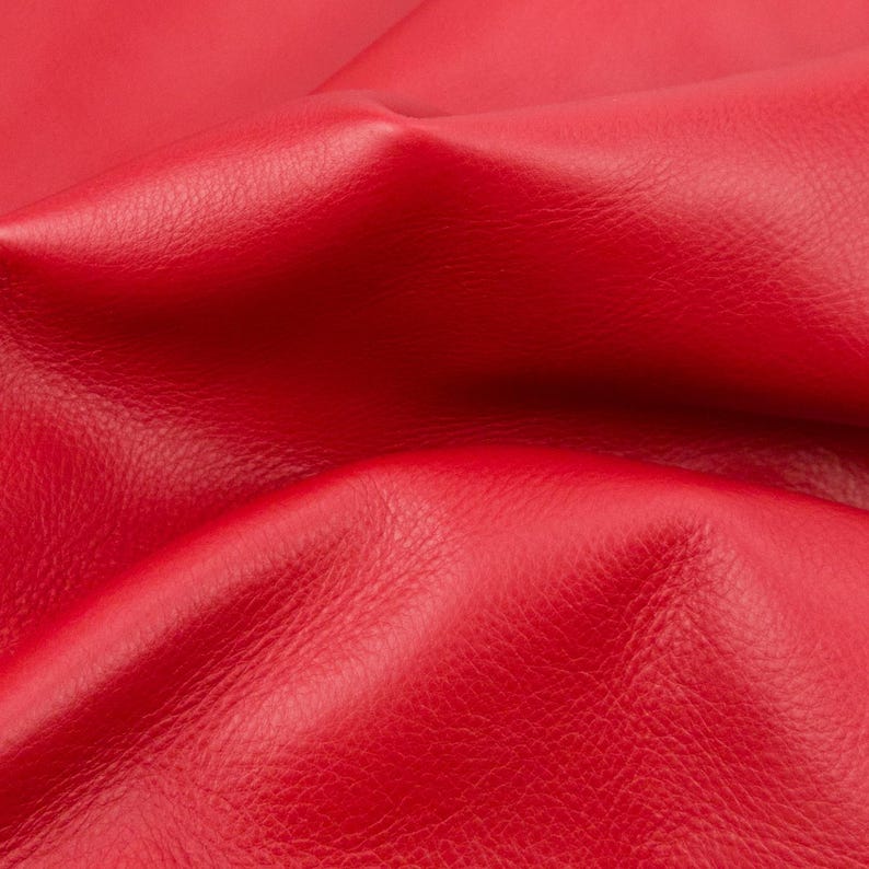 Puede incluir: Un material de color rojo vibrante con una textura de grano natural distintiva. La superficie est&aacute; plegada y drapeada, creando curvas suaves y onduladas con sombras profundas que resaltan la flexibilidad de esta superficie roja texturizada.
