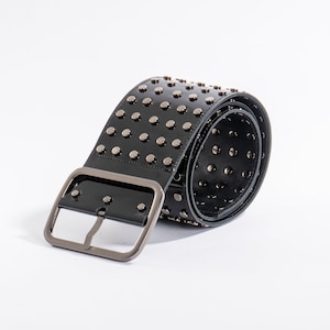 May include: A wide black belt with a glossy finish, featuring multiple rows of silver-toned metal studs across the surface. The belt includes a large, rectangular silver-toned metal buckle and is coiled to show the interior and exterior details.