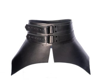 May include: A wide black corset belt featuring two horizontal straps across the front, each secured with a rectangular metal buckle and multiple adjustment holes. The structure is rigid with a flared, pointed hemline and smooth finish.