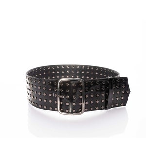 May include: A wide black belt featuring a glossy finish and multiple rows of small, dark metallic studs. The belt is secured with a rectangular silver-toned metal buckle and includes a matching black belt loop to hold the end of the strap in place.