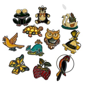 May include: A selection of colourful metal charms in various animal and object shapes. The charms include a frog, teddy bear, turtle, owl, bird, whale, butterfly, strawberries, swans, a girl, and a parrot.