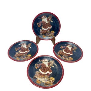 May include: A set of four decorative Christmas plates featuring a Santa Claus design. The plates have a dark blue background with a red rim and a Santa Claus illustration surrounded by teddy bears.