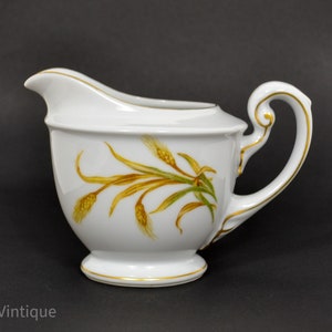 May include: White porcelain creamer with a gold rim and a delicate floral design featuring wheat stalks in shades of yellow and green.
