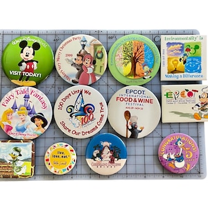 Pode incluir: Uma coleção de dez botões redondos e coloridos do Disney World. Os botões apresentam vários personagens, logotipos e eventos, incluindo o Mickey Mouse, um castelo de conto de fadas e o Festival Internacional de Comida e Vinho do Epcot.