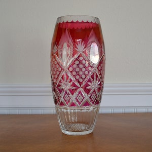 May include: A tall, clear glass vase with a red, cut-glass design. The vase has a scalloped rim and a diamond-shaped pattern.