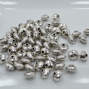 May include: A large quantity of silver-toned metal beads with a decorative design. The beads are round and have a flat top and bottom.