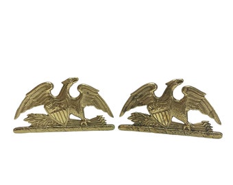 May include: A pair of gold-toned metal eagle bookends. Each eagle is perched on a branch with its wings spread. The eagles are facing each other and have a shield on their chest.
