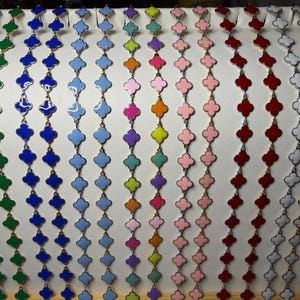 May include: A collection of long necklaces featuring a repeating clover-shaped motif in various solid colors including green, blue, light blue, purple, pink, orange, red, and white, all connected by thin gold-toned metal links in a vertical arrangement.