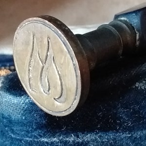 Puede incluir: Sello de cera metálico antiguo con mango de madera. El sello presenta un diseño ovalado con las iniciales "LS" en una fuente estilizada. El sello está sobre una superficie de terciopelo azul oscuro.