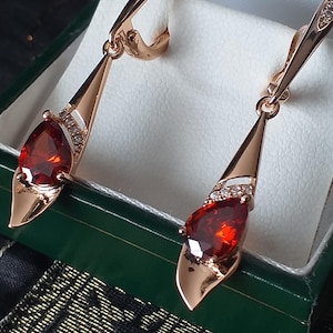 Peut inclure: Une paire de boucles d'oreilles pendantes en or rose avec des gouttes de pierres précieuses rouges et des accents de cristal transparent.