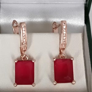 Puede incluir: Un par de pendientes de oro rosa con piedras preciosas rectangulares de color rojo intenso. Los pendientes tienen un cierre de palanca y se presentan en una caja con forro de satén blanco. La parte superior de los pendientes tiene una fila de pequeñas piedras transparentes.