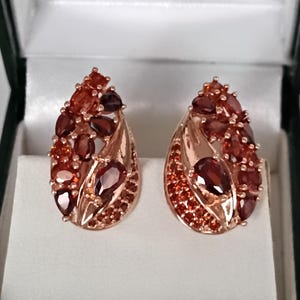 Peut inclure: Une paire de boucles d'oreilles en forme de goutte d'eau avec un sertissage en or rose. Chaque boucle d'oreille est ornée d'un groupe de pierres précieuses rouges et oranges de différentes tailles. Présentées dans un écrin blanc.