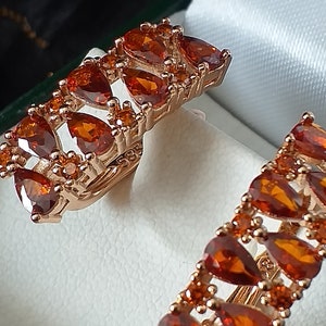 Puede incluir: Un par de pendientes de oro con piedras preciosas de color naranja en forma de lágrima. Los pendientes están engastados en una delicada banda de oro y tienen un acabado pulido.