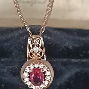 Può includere: Una collana con pendente in oro rosa caratterizzata da una gemma centrale ovale color rosa intenso circondata da un alone di piccole pietre chiare. Il pendente presenta una contromaglia traforata con una pietra chiara e una catena abbinata.