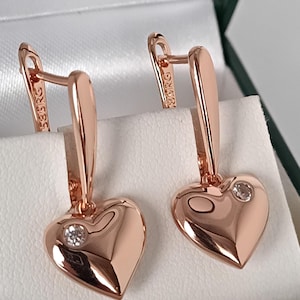 Peut inclure: Paire de boucles d'oreilles en forme de cœur en or rose, chacune ornée d'un petit diamant. Les boucles d'oreilles sont présentées dans un écrin blanc. Finition polie, fermoirs à levier. Le métal est estampillé "585RG".