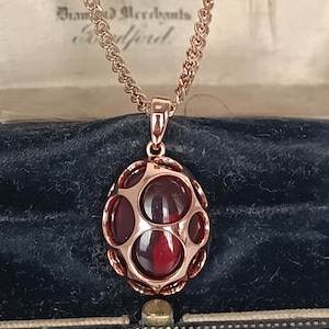May include: A rose gold pendant necklace with a distinctive design. The pendant showcases red, oval-shaped stones set in a rose gold frame. The necklace is presented in a vintage jewellery box.