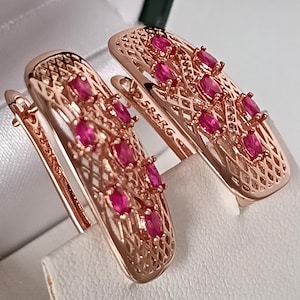 May include: Rose gold earrings with a lattice design, each set with oval-shaped, bright pink gemstones. The earrings have a lever back closure. The text "585RG" is visible on one earring.