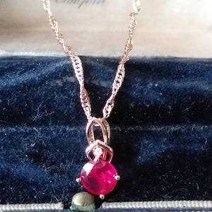 Könnte beinhalten: Eine Halskette aus roségoldener Kette mit einem Anhänger mit einem roten Edelstein. Die Halskette befindet sich in einer samtenen Schachtel mit der Aufschrift "Falkner & Sons Ltd Diamond Merchants Bradford".