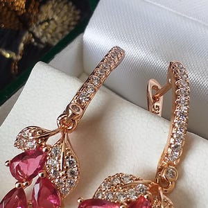Op de afbeelding: Een paar rosé gouden oorringen met hangende roze edelstenen en heldere zirkonia stenen.