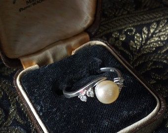 May include: A white pearl ring with small diamonds set in a silver band, inside a brown velvet ring box with the inscription "Hancock & Son (Goldsmiths) Ltd. 29 King Street & St. Ann's Passage Manchester Phone: BLACKFRIARS 4512"