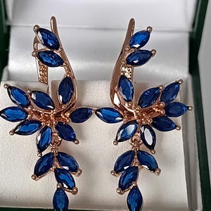 Peut inclure: Paire de boucles d'oreilles en or rose avec un motif floral. Chaque boucle d'oreille présente de multiples pierres précieuses bleu foncé taillées en marquise, disposées pour ressembler à des feuilles et des pétales. Les boucles sont dans un écrin vert et blanc.