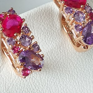 Pode incluir: Um par de brincos em ouro rosa com um conjunto de pedras preciosas rosa e roxas. Os brincos apresentam uma combinação de pedras ovais e redondas. Apresentados numa superfície branca.